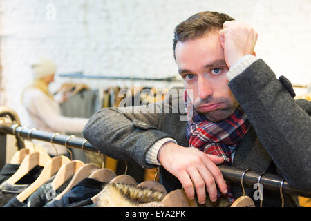 Vista di un giovane uomo informale in attesa mentre la moglie di shopping Foto Stock