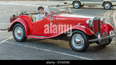 Un rosso vintage MG sport auto parcheggiate in Teignmouth, Devon, con il proprietario in posa e sorridente per l'immagine. Foto Stock