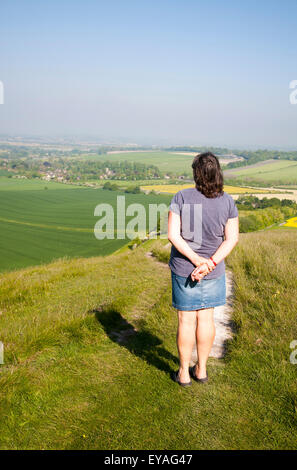 Donna in piedi sulla ripida scarpata chalk Cherhill pendenza verso il basso, Wiltshire, Inghilterra, Regno Unito guardando verso il villaggio di Cherhill Foto Stock