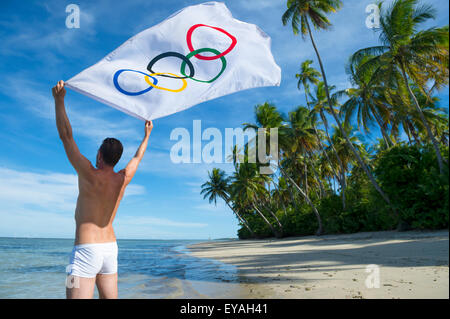 BAHIA, Brasile - MARZO 18, 2015: atleta sorge su rustico spiaggia brasiliana holding bandiera olimpica nel vento. Foto Stock