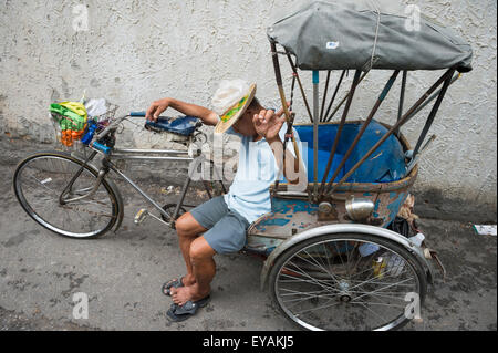 CHIANG MAI, Thailandia - Novembre 07, 2014: Driver di una bicicletta tradizionale rickshaw prende un pisolino su una tranquilla strada laterale. Foto Stock