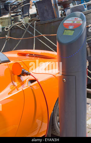 Orange Tesla auto sportiva essendo addebitato al pubblico la stazione di carica. Amsterdam Olanda Foto Stock