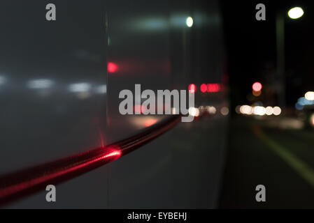 Un'immagine ravvicinata di una corda rossa luce andando lungo una parete al di fuori di una zona di costruzione di notte con le automobili" luci di coda sfocate Foto Stock