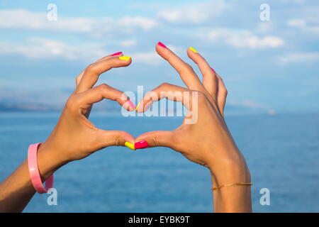 Forma di cuore facendo delle mani contro il mare e il cielo guardando l'acqua Foto Stock