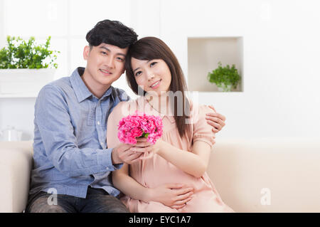 Giovane uomo e donna incinta azienda fiori e sorridente alla telecamera, Foto Stock