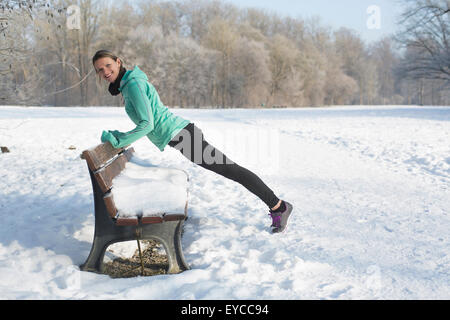 Giovane donna stiramento nella coperta di neve park Foto Stock