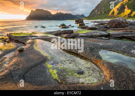 Drammatico tramonto sulla spiaggia di Uttakleiv sulle isole Lofoten in Norvegia con uno stagno naturale in primo piano. Hdr elaborato. Foto Stock