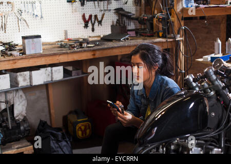 Meccanico femmina tramite cellulare in officina Foto Stock