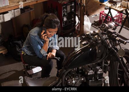 Meccanico femmina tramite cellulare in officina Foto Stock