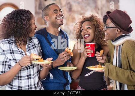 Quattro amici adulti a ridere e mangiare piatti per le feste in cucina Foto Stock