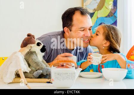 Ragazza baciare padre sulla guancia a tavola Foto Stock