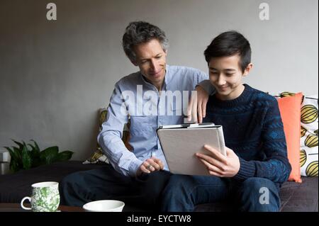 Padre e figlio adolescente la lettura digitale compressa sul divano Foto Stock