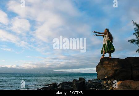 Donna hula sulla parte superiore delle rocce costiere indossando il costume tradizionale, Maui, Hawaii, STATI UNITI D'AMERICA Foto Stock