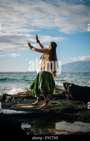Giovane donna hula sulle rocce costiere indossando il costume tradizionale, Maui, Hawaii, STATI UNITI D'AMERICA Foto Stock