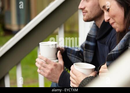 Ritagliato colpo di coppia giovane seduto sul portico passo a bere caffè Foto Stock