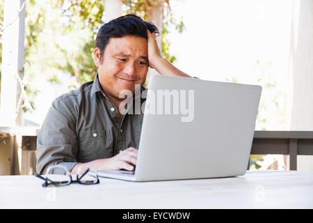 Frustrati imprenditore maturo lavorando sul computer portatile in veranda Foto Stock