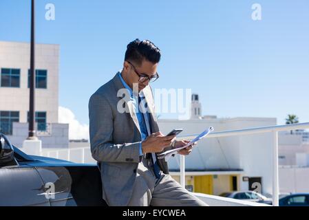 Giovane imprenditore nel city car park la lettura di testi dello smartphone Foto Stock