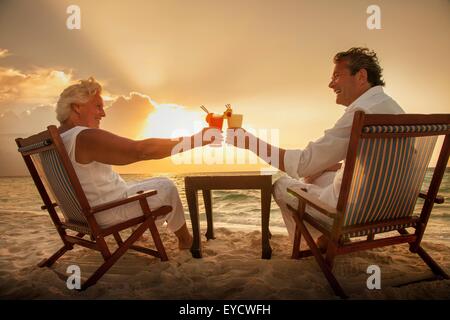 Coppia senior tostare bevande sulla spiaggia, Maldive Foto Stock