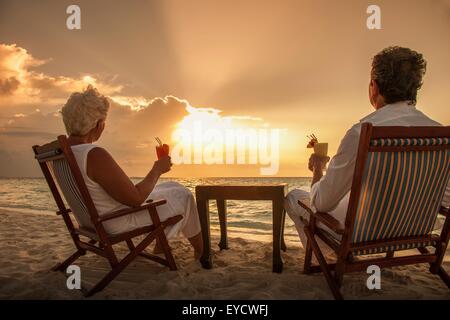 Coppia senior con bevande sulla spiaggia, Maldive Foto Stock