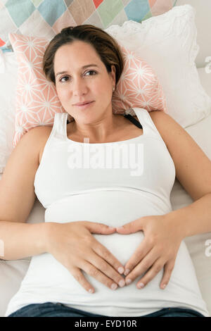 Donna incinta messa a forma di cuore sulla stomaco Foto Stock