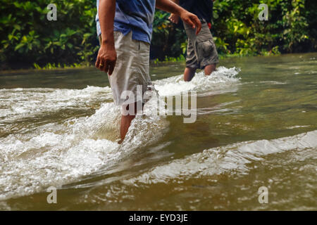 Uomini che camminano su un flusso rapido poco profondo nel mezzo della foresta consueta vicino alla più lunga della tradizionale comunità IBAN Dayak a Kapuas Hulu, Indonesia. Foto Stock