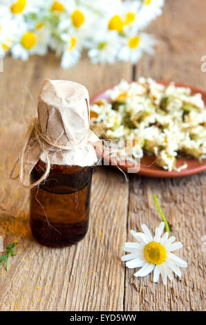 Margherite e prodotti di camomilla (aroma essenziale olio e fiori secchi) oltre rustico sfondo di legno Foto Stock