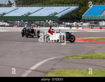Chris Pearson onde per la folla dopo la finitura del Trofeo Kidson per pre-era auto sportive, nella sua 1935, Austin sette, durante la Silverstone Classic. Foto Stock