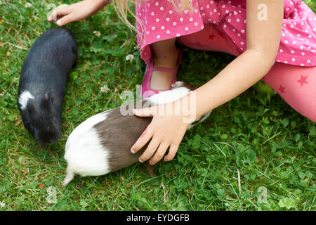 Bambino ragazza rilassante e giocare con il suo cavie esterno su erba verde prato e giardino, campagna, estate, animali domestici, animali Foto Stock