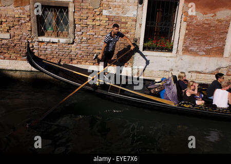 Un gondoliere calci contro una parete a raddrizzare la sua gondola durante un giro in uno stretto canale a Venezia, Italia. Prezzi correnti (2015) è di 80 Euro per 40 minuti di viaggio (guadagnare circa 130.000 euro all'anno) lungo le vie navigabili di questa vecchia città ma non raramente gondolieri indossare la loro paglia navigante hat. Foto Stock