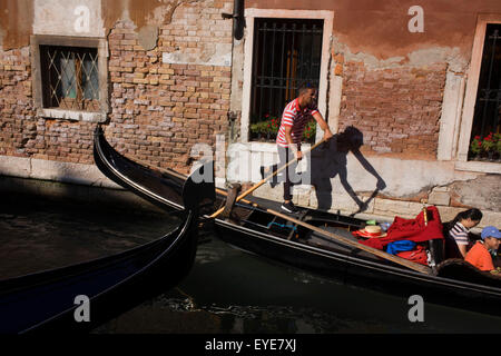 Un gondoliere calci contro una parete a raddrizzare la sua gondola durante un giro in uno stretto canale a Venezia, Italia. Prezzi correnti (2015) è di 80 Euro per 40 minuti di viaggio (guadagnare circa 130.000 euro all'anno) lungo le vie navigabili di questa vecchia città ma non raramente gondolieri indossare la loro paglia navigante hat. Foto Stock