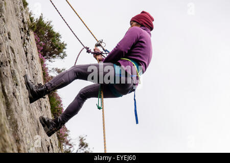 Female Rock scalatore la discesa in corda doppia giù con la fune di sicurezza e cablaggio di arrampicata su un rockface. Snowdonia, il Galles del Nord, Regno Unito, Gran Bretagna Foto Stock