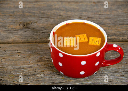 Minestra di pomodoro e formaggio cracker in una zuppa rossa mug con pois su legno rustico. Foto Stock