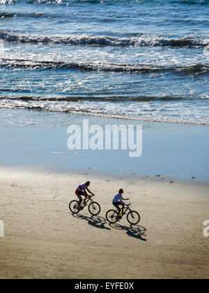 La mattina presto la luce solare getta ombre di due piloti di bicicletta al Crystal Cove in Newport Beach, CA. Nota heavy surf. Foto Stock