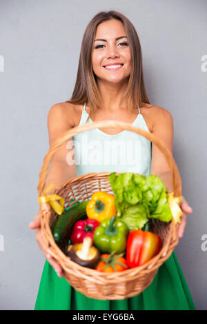 Ritratto di un bel giovane donna cestello di contenimento con verdure su sfondo grigio Foto Stock