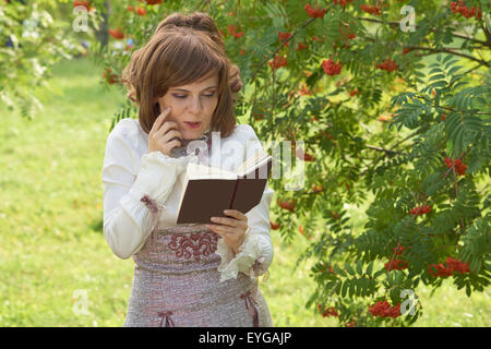 Ragazza sorridente legge libri interessanti vicino a rowan tree in estate Foto Stock