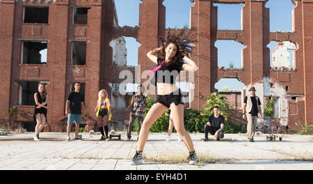 Ragazza giovane hip hop in una piazza con i suoi amici il suo supporto. La luce naturale del sole su edifici ad alta. Foto Stock