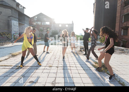 Energici giovani hip hop ballerini di strada di svolgere la loro routine in una piazza urbana retroilluminati da un sole luminoso flare su hig Foto Stock