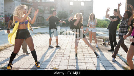 Energici giovani hip hop ballerini di strada di svolgere la loro routine in una piazza urbana retroilluminati da un sole luminoso flare su hig Foto Stock