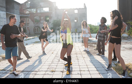 Energici giovani hip hop ballerini di strada di svolgere la loro routine in una piazza urbana retroilluminati da un sole luminoso flare su hig Foto Stock