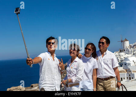 Turisti asiatici che scattano selfie su smartphone fotocamera Selfie Stick persone telefono di gruppo fare foto amici Isole greche Oia Santorini Grecia Europa Foto Stock