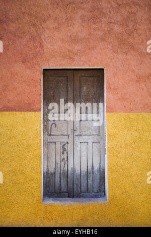 Vista esterna del vecchio weathered porta di legno centrato in stucco parete dipinta Terracotta e oro. Foto Stock