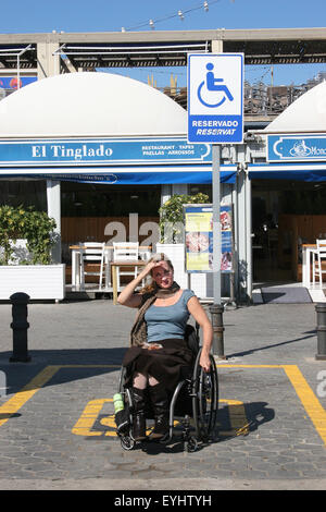 Donna che utilizza una sedia a rotelle in un parcheggio disabili spot Foto Stock