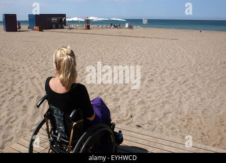 Una donna su una sedia a rotelle godendo di un pomeriggio di sole in spiaggia Foto Stock