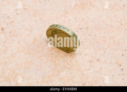 Unico British pound coin in piedi sul bordo sul pavimento Foto Stock