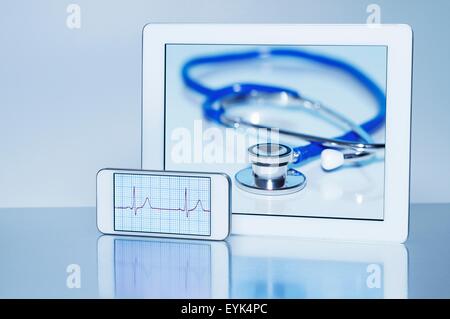 Smart phone visualizzando un elettrocardiogramma e tavoletta digitale visualizzazione di uno stetoscopio acustico, still life Foto Stock