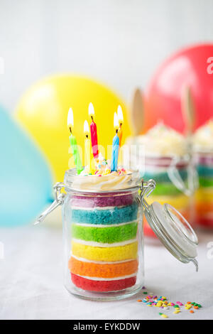 Rainbow layer cake in un vaso con candele di compleanno Foto Stock