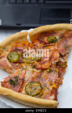 Pezzi di pizza con salsicce e pancetta nella piastra sulla tastiera portatile sfondo Foto Stock