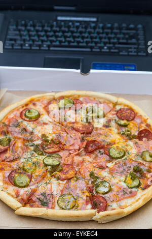 Pezzi di pizza con salsicce e bacon in scatola sul laptop sullo sfondo della tastiera Foto Stock