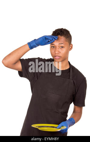 Ispanico giovane uomo blu da indossare guanti di pulizia tenendo la piastra verde cercando stanchi di espressione del viso verso la telecamera Foto Stock