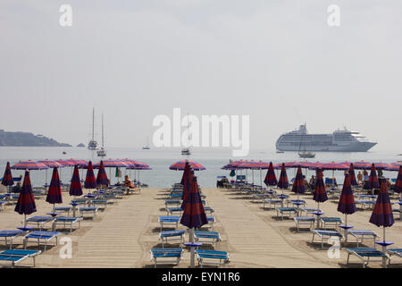 Spiaggia italiana con righe vuote di lettini per il sole e la nave da crociera sette mare Mariner al di ancoraggio Foto Stock